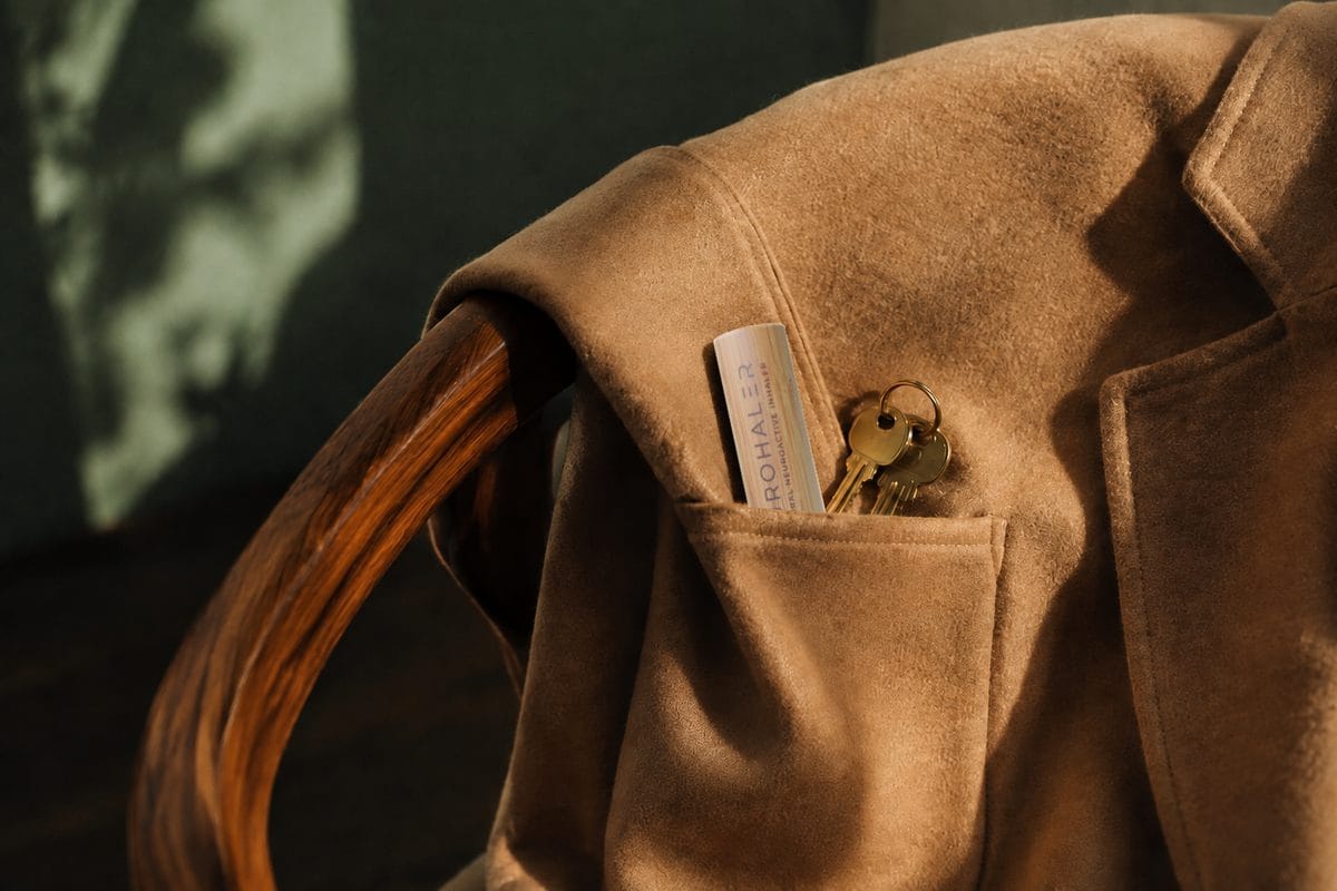 A capped bamboo Neurohaler and brass keys sit in the pocket of a camel wool coat.